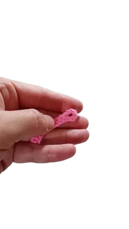 A hand holding a small piece of pink fabric for a crochet pumpkin pattern, featuring a hole at one end.