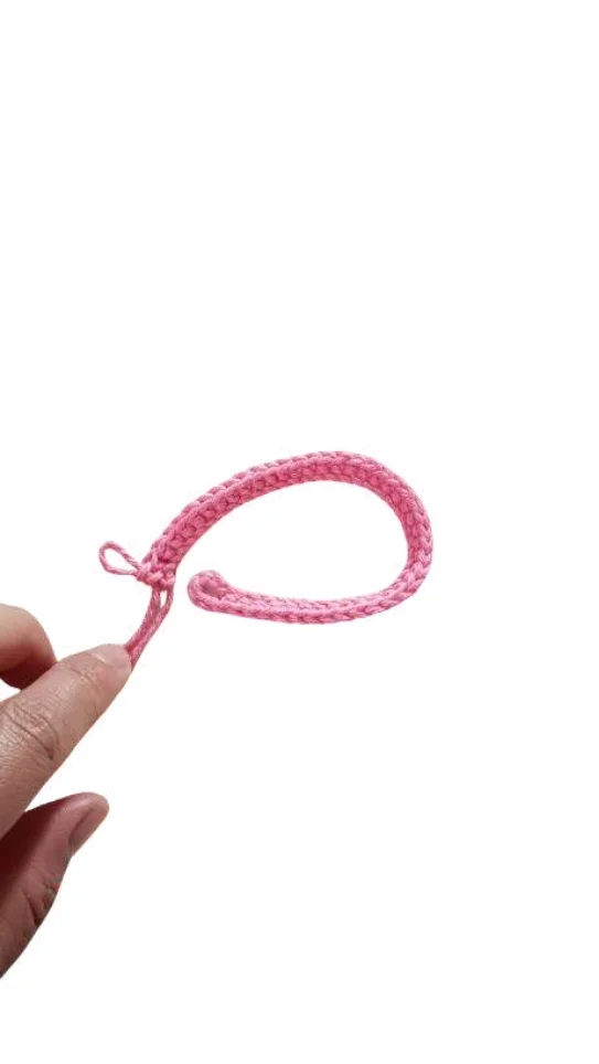 A hand holds a pink crocheted cord shaped into a loop for a giraffe amigurumi.