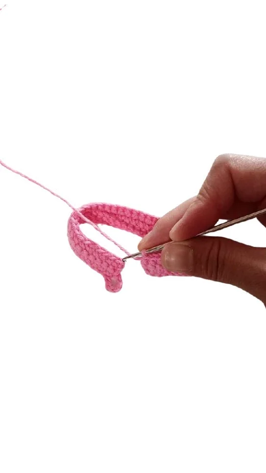 A hand uses a crochet hook to join the ends of a pink strip for a pumpkin crochet pattern.