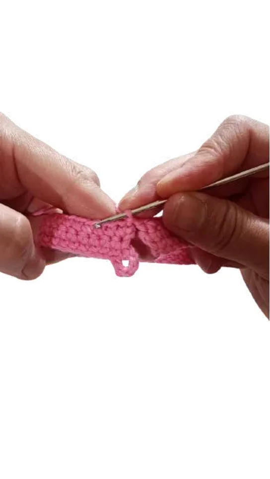 Hands hold a crochet hook while working on a pink yarn giraffe amigurumi.