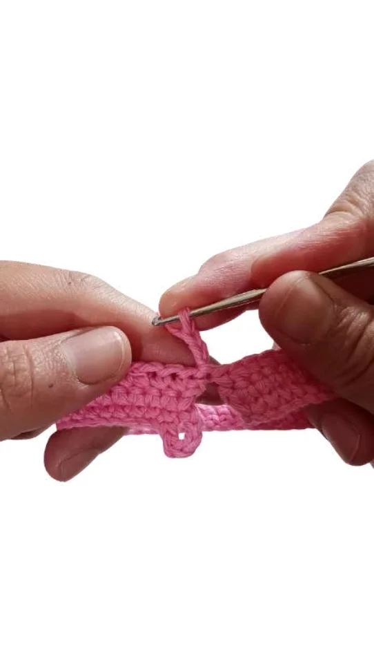 Hands using a crochet hook to work pink yarn into a chain stitch for a free crochet pumpkin pattern.