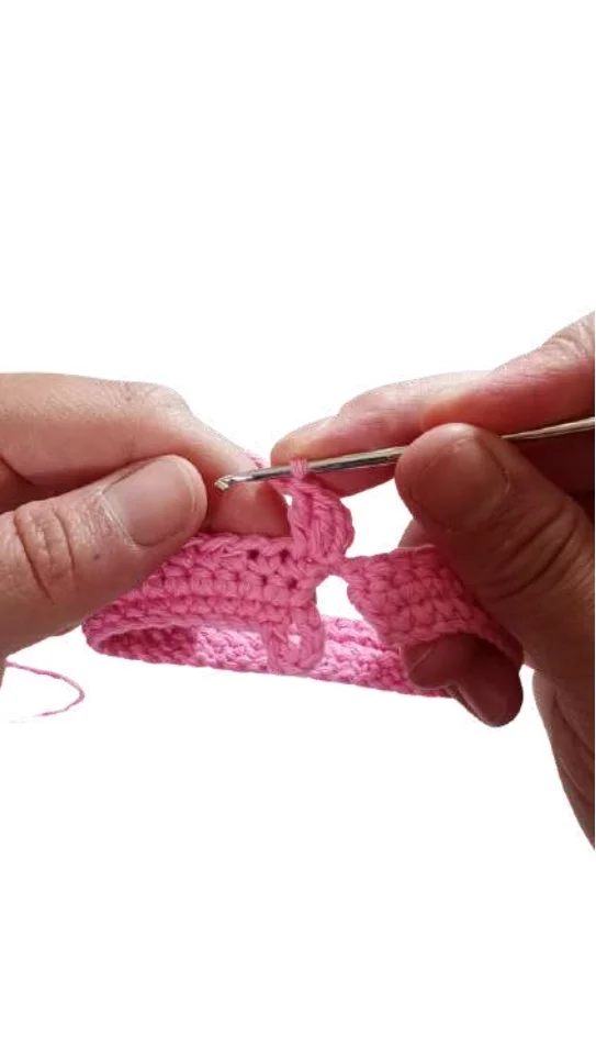 Hands using a crochet hook to work pink yarn for a crochet pumpkin pattern.