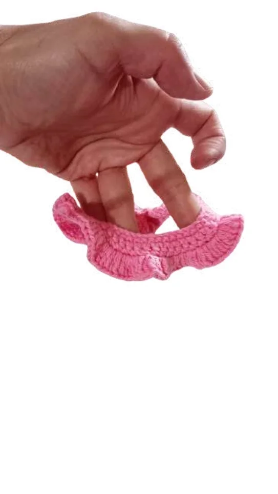 A hand holds a small pink crocheted ruffle hair scrunchie, styled much like a free crochet pumpkin pattern.