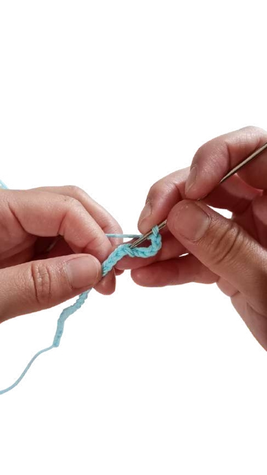 Hands using a crochet hook to work with light blue yarn for a crochet pumpkin pattern.