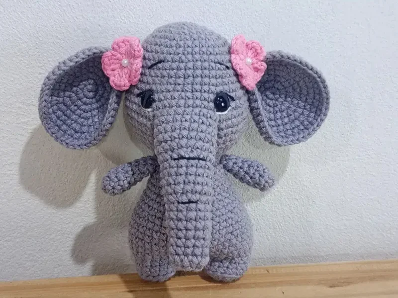 Crocheted gray elephant amigurumi plush toy with pink flower accents on its ears.